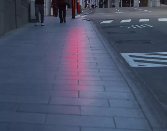 Photo capturing a sidewalk and street with the glow of a red traffic light reflecting on the pavement