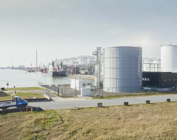 Truck driving past the Schelde canal and storage tanks in the Port of Antwerp