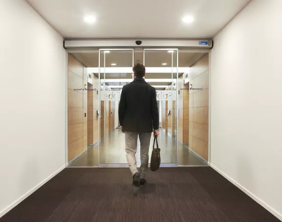 Man about to walk through a sliding glass door towards the elevator corridor at Stibbe in Brussels