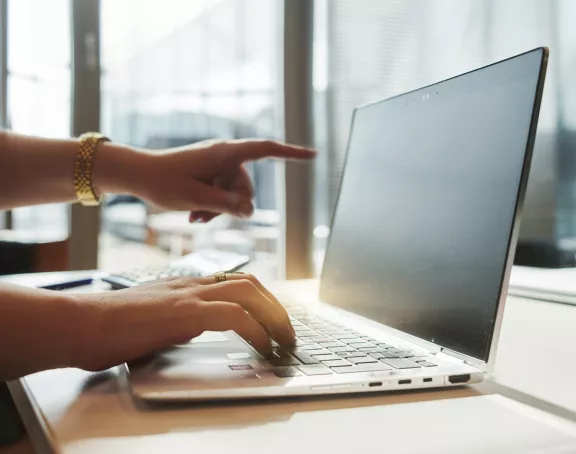 Close-up of a woman's hands with her right hand placed on her laptop keyboard and her left hand pointing at her laptop screen