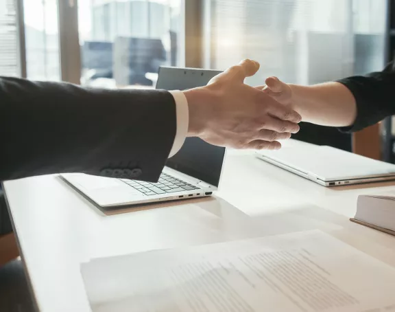 Cropped close-up of two business people sitting opposite each other at a conference table and shaking hands over the table