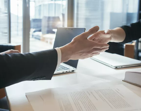 Cropped close-up of two business people sitting opposite each other at a conference table and shaking hands over the table