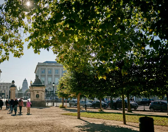 Brussels park scene featuring vibrant green trees, people casually strolling, and the prominent presence of the Palace of Justice amidst other historic architecture in the background