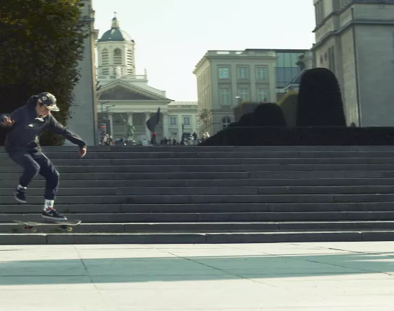 Child doing a skateboard trick on the steps at Mont des Arts in Brussels, with Place Royale in the background