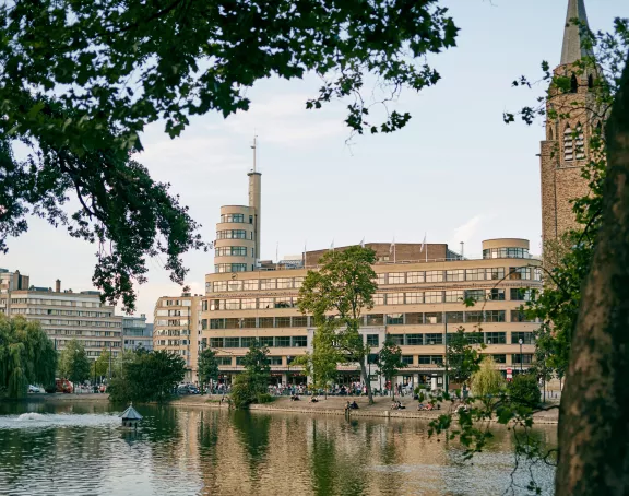 Flagey building viewed from across water, surrounded by vibrant green trees