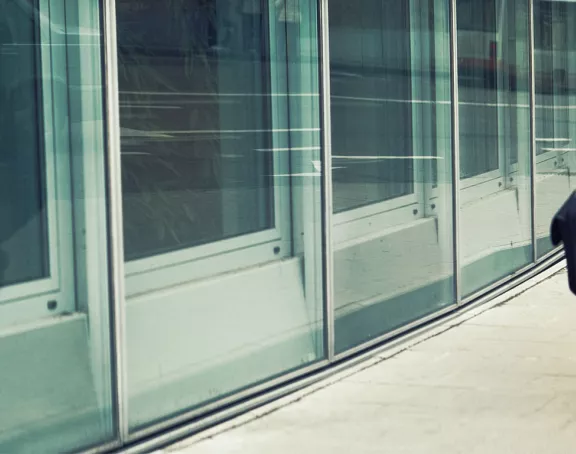 Business man walking by the glass Central Plaza building in Brussels, with his reflection visible in the window