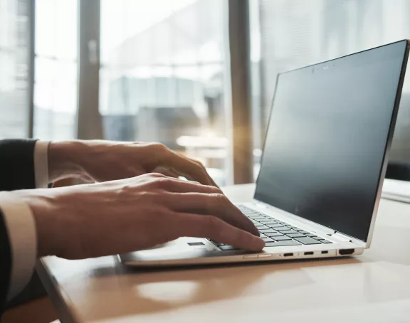 Close-up of a man's hands typing on a laptop keyboard