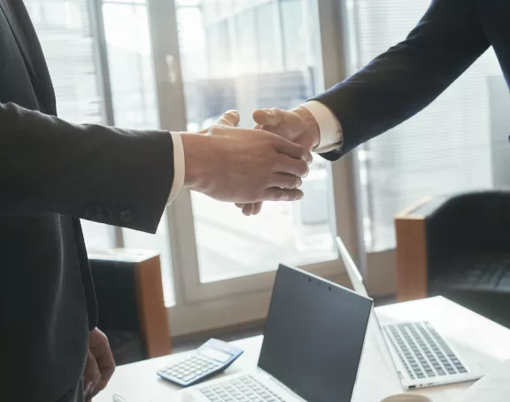 Cropped close-up of two business people standing around a conference table and shaking hands over the table