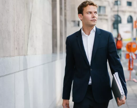 Male Stibbe lawyer walking down Rue de Loxum in Brussels and holding a laptop and papers