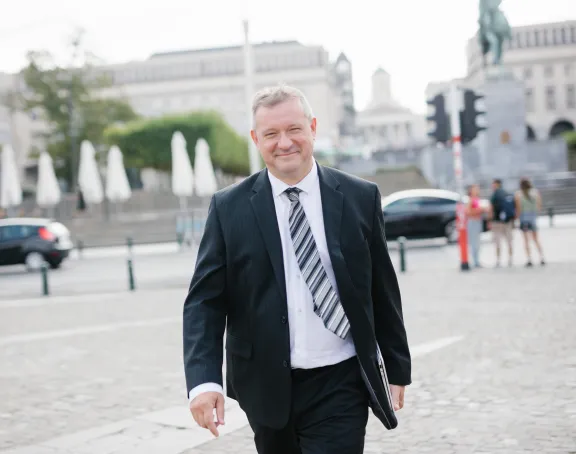 Male Stibbe employee walking in front of Mont des Arts in Brussels smiling at the camera and holding his laptop in his left hand