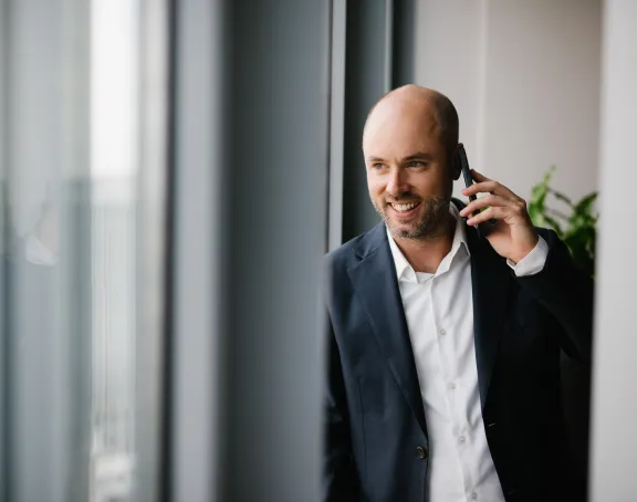 Male Stibbe lawyer smiling while talking on the phone and looking out the window in a meeting room at Stibbe in Brussels