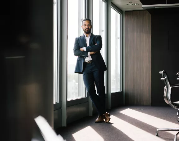 Male Stibbe lawyer looking at the camera while standing confidently against the window in a meeting room at Stibbe in Brussels