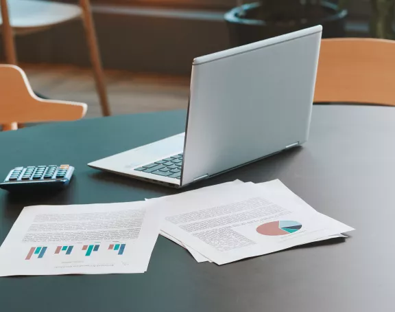 Office table with papers, pens, a laptop and calculator