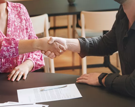 Cropped close-up of two people sitting at a table and shaking hands