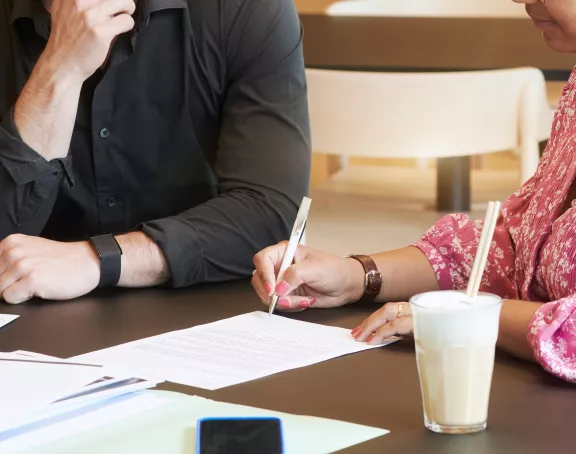 Cropped close-up of two people having a seated meeting where the woman is taking notes