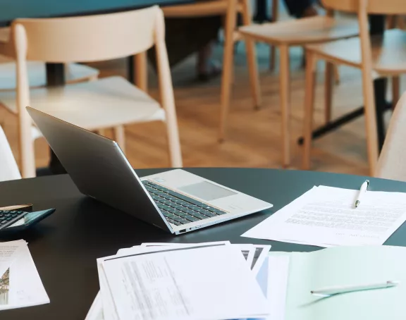 Office table with papers, pens, a laptop and calculator