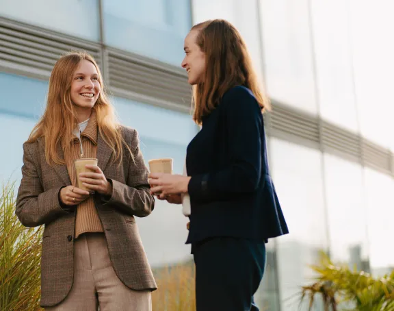 Two women engaged in a friendly conversation on the rooftop terrace of Stibbe in Brussels, both holding cups of coffee.