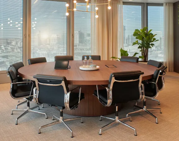 Modern conference room at Stibbe with a round wooden table, black leather chairs, large windows and a TV screen.