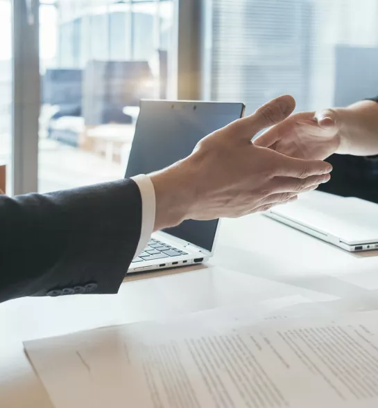 Cropped close-up of two business people sitting opposite each other at a conference table and shaking hands over the table