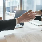 Cropped close-up of two business people sitting opposite each other at a conference table and shaking hands over the table