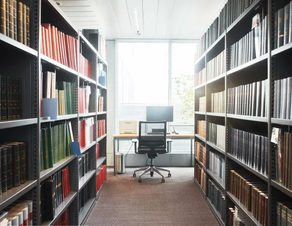 Library corridor with stocked bookcases on both sides and a desk at the end of the corridor at Stibbe in Brussels