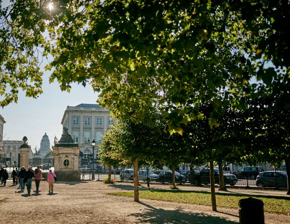 Brussels park scene featuring vibrant green trees, people casually strolling, and the prominent presence of the Palace of Justice amidst other historic architecture in the background