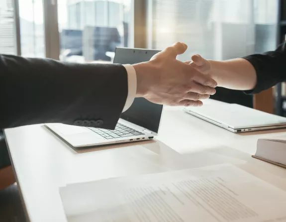 Cropped close-up of two business people sitting opposite each other at a conference table and shaking hands over the table