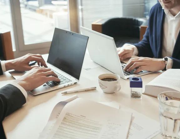 Cropped close-up of two business people sitting opposite each other at a conference table and working on their laptops