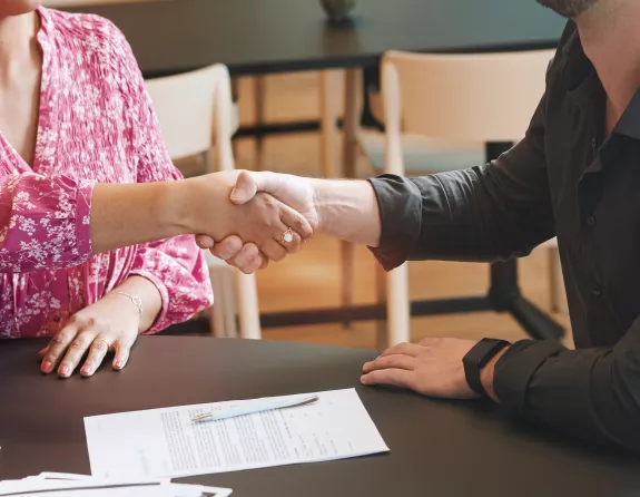 Cropped close-up of two people sitting at a table and shaking hands