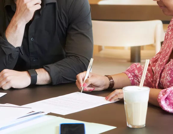 Cropped close-up of two people having a seated meeting where the woman is taking notes