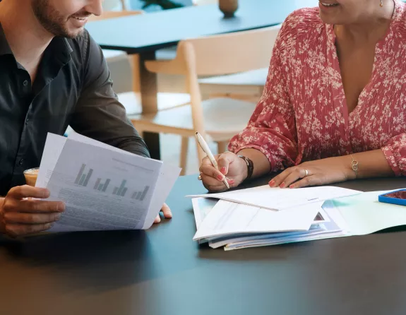 Cropped close-up of two people looking at papers while having a seated meeting