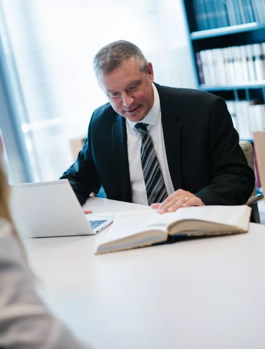 Male Stibbe employee looking in a book while having a chat with a female colleague in the library of Stibbe in Brussels