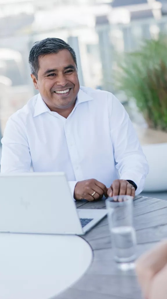 Male Stibbe employee sitting with his laptop at a table and having a laugh with a female colleague on the rooftop terrace at Stibbe in Brussels