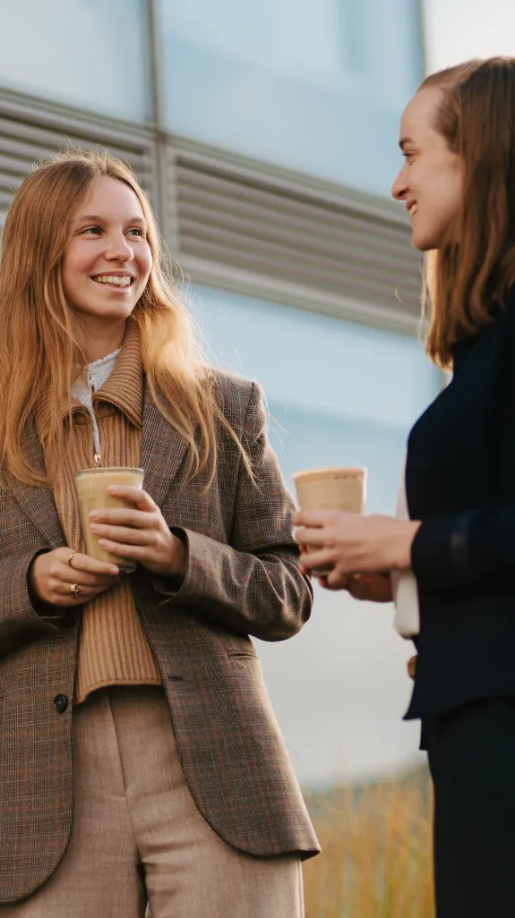 Two women engaged in a friendly conversation on the rooftop terrace of Stibbe in Brussels, both holding cups of coffee.