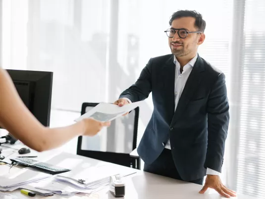 Male Stibbe lawyer standing at his office desk and handing over a paper to a colleague