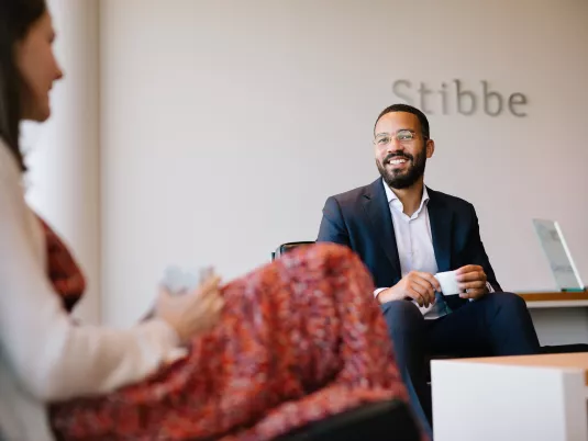 Male Stibbe lawyer in business suit smiling while chatting with a female colleague at the reception of Stibbe in Brussels