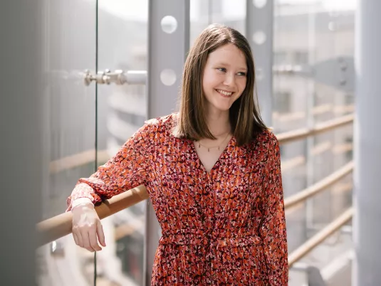 Female Stibbe employee glancing to the side with a smile, casually leaning against a terrace railing