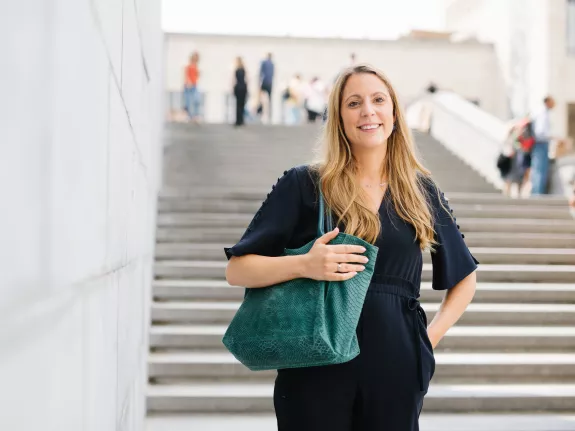 Female Stibbe lawyer posing with a bag over her shoulder and smiling at the camera while standing on the stairs at the Mont des Arts in Brussels