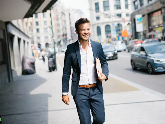 Male Stibbe lawyer walking happily past the Central Station in Brussels with a case file under his arm