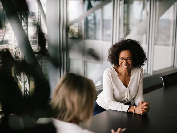 Two female Stibbe employees laughing while having a chat with each other in a meeting room at Stibbe in Brussels