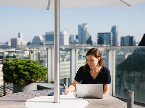 Female Stibbe lawyer taking notes in front of her laptop at the rooftop bar of Stibbe in Brussels